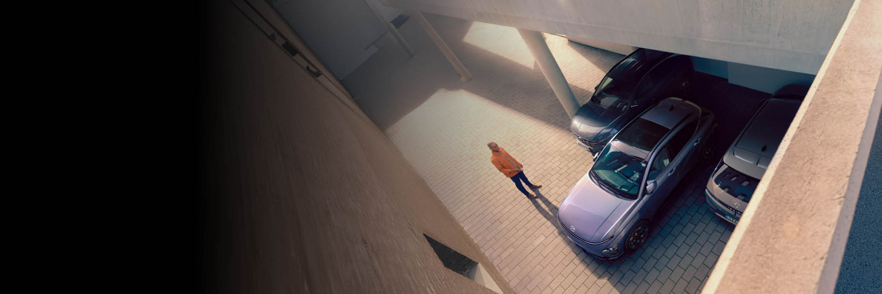 In einer Parkgarage steht eine Person neben mehreren geparkten Autos und wird von oben fotografiert.