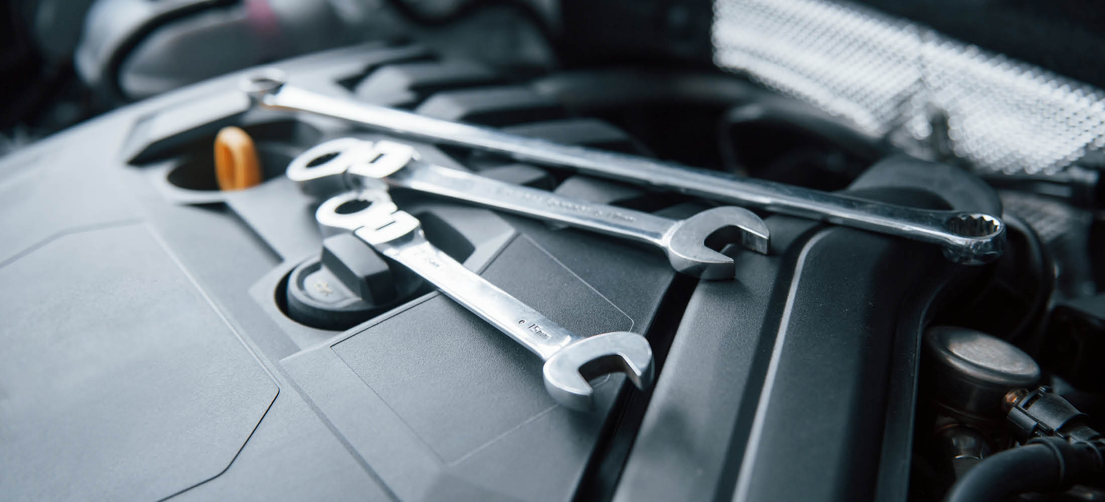 Drei silberne Schraubenschlüssel liegen auf einem Motorblock im Inneren eines Autos. Die Szene deutet auf eine Reparatur oder Wartung des Fahrzeugs hin.