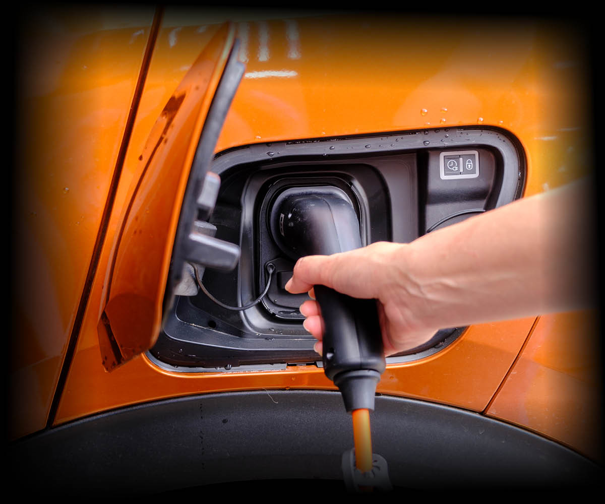 Eine Hand steckt ein Ladekabel in die Ladebuchse eines orangefarbenen Elektroautos.