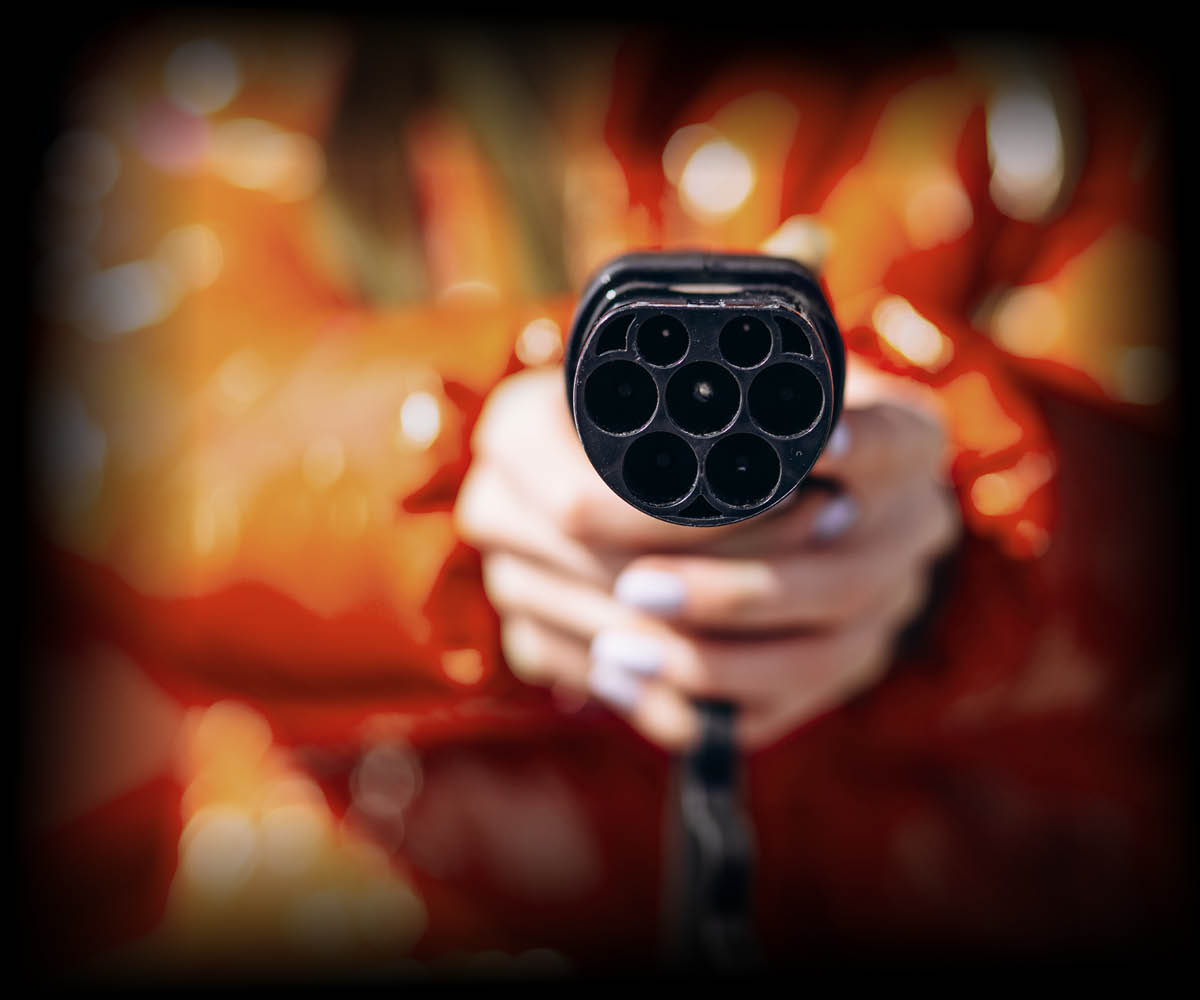 Person, die ein Ladekabel für ein Elektroauto in der Hand hält und auf die Kamera richtet. 