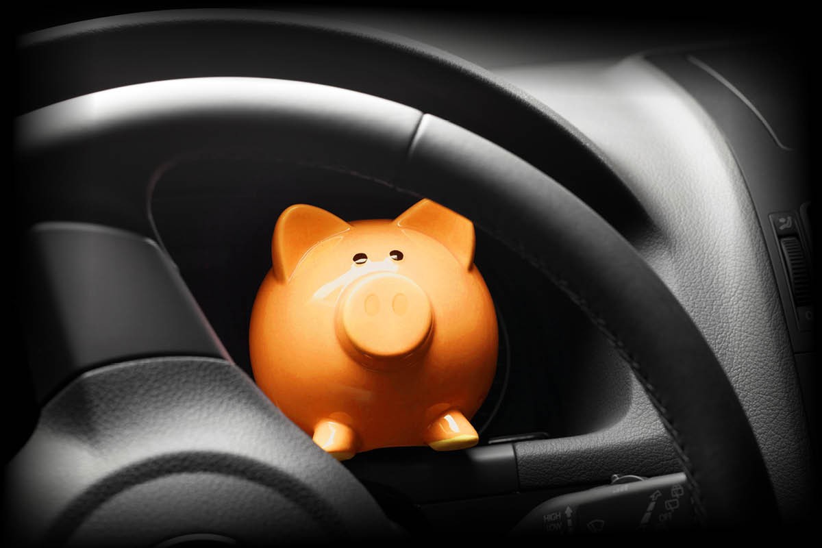 Sparschwein, das auf dem Armaturenbrett eines Autos hinter dem Lenkrad steht.