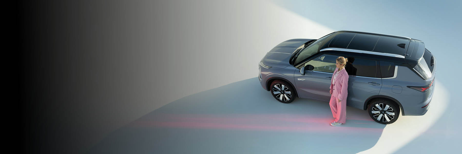 Eine Frau steht neben einem grauen SUV auf einer hellen Fläche.