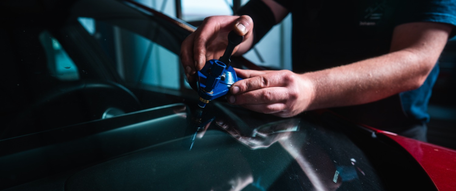 Eine Person repariert mit einem Spezialwerkzeug einen Steinschlag oder Riss an einer Autoscheibe.
