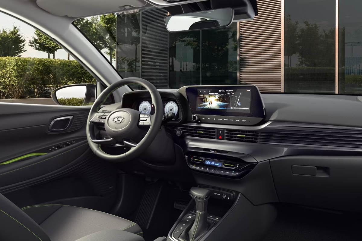 Multifunktionslenkrad vor digitalen Rundinstrumenten, großer Touchscreen auf dem Armaturenbrett, darunter Lüftungsschlitze und Klimabedienung. Unten ein Automatik-Wählhebel. Schwarze Sitze und Türverkleidungen mit grünen Ziernähten.