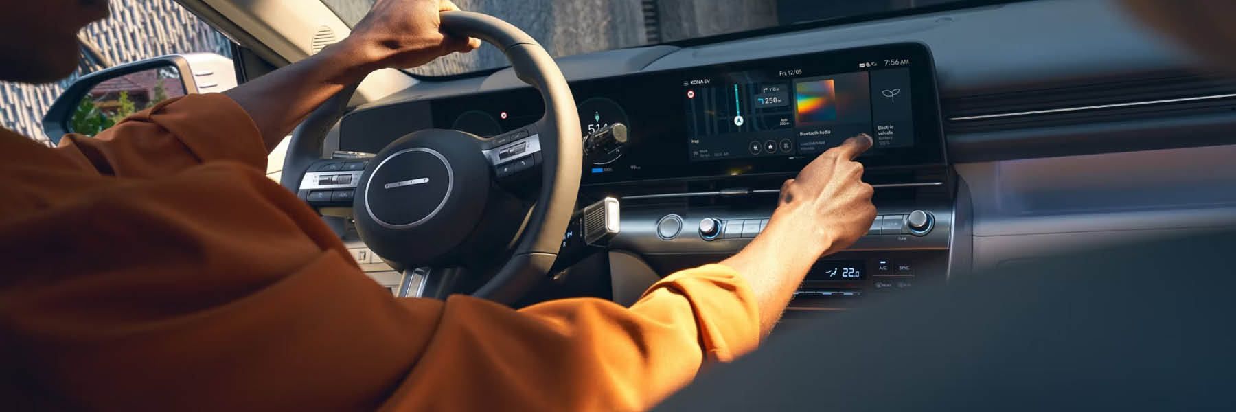 Eine Person bedient das große Touchdisplay eines modernen Autos während der Fahrt und hält mit der anderen Hand das Lenkrad.