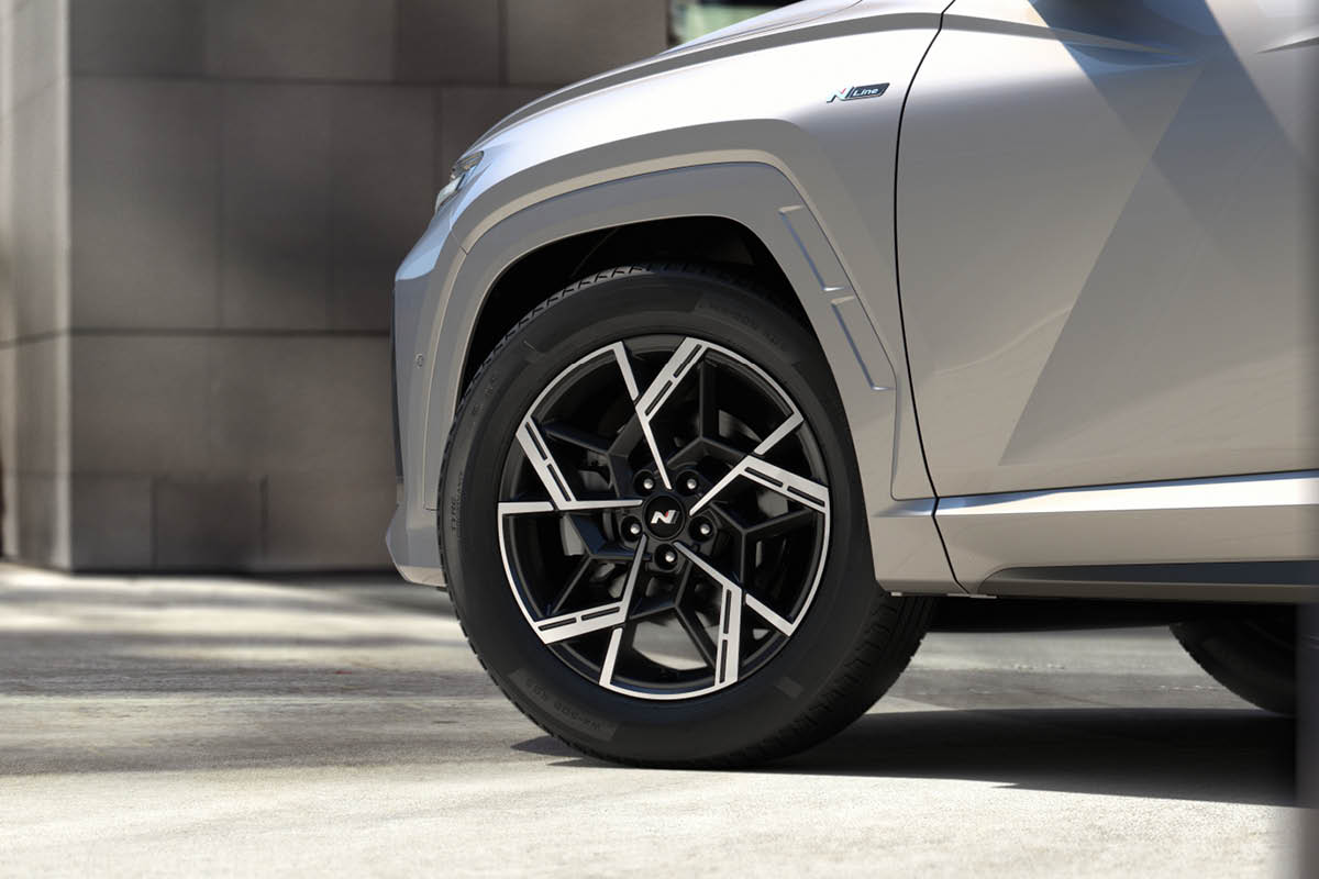 Nahaufnahme eines Autos: zu sehen ist das vordere Rad mit sportlicher, schwarz-silberner Alufelge und Reifen. Am Kotflügel steht ein „N Line“-Badge; die Karosserie ist silbern.
